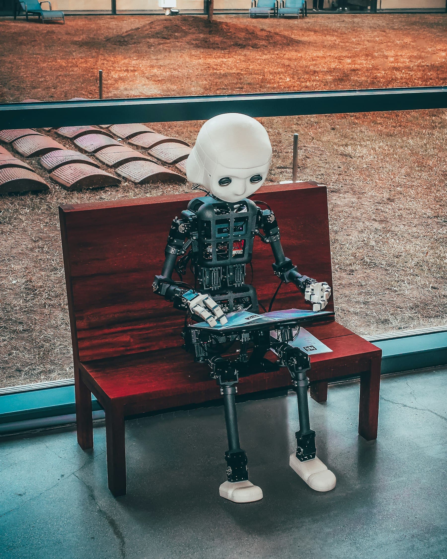 Humanoid robot sitting on a wooden bench, reading a book